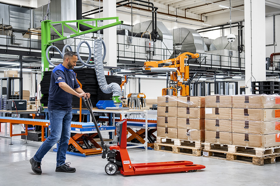 A person picks up a pallet loaded with boxes using a pallet truck